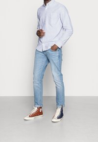 Ljust blå randig skjorta med knappar, ljusblå jeans och tvåfärgade högstövlar i brunt och marinblått. Slät tyg, avslappnad passform.