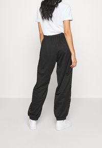 Svarta joggers med en avslappnad passform, elastisk midjeband och sidodetaljer med snörning. Mjuk tyg med smalnade muddar vid anklarna. Parat med en vit t-shirt.