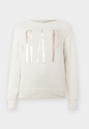 Krēmkrāsas garām piedurknēm krekls ar metālisku zelta "GAP" uzrakstu krūtīs, ar ribotām piedurknēm un apakšmalu.