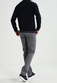 Mörkblå långärmad skjorta med vit kant som bärs tillsammans med grå byxor och mörkblå sneakers. Outfiten har en figurnära design med släta texturer.