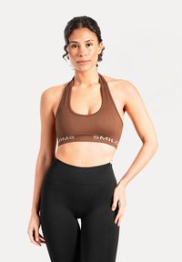 Brązowy prążkowany sportowy biustonosz z zaokrąglonym dekoltem i halterowymi ramiączkami. Na pasie biała napisana litera "SMIL". Do kompletu czarne legginsy z wysokim stanem.