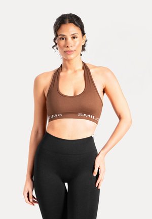 Reggiseno sportivo marrone a coste con scollo a U e spalline a canottiera. Presenta la scritta bianca "SMIL" lungo la fascia. Abbinato a leggings neri a vita alta.