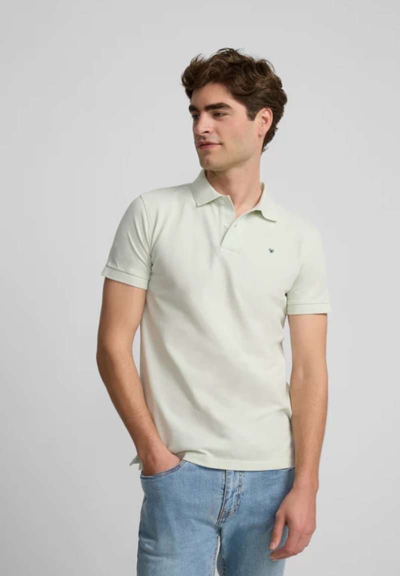 Polo shirt verde chiaro in cotone, con colletto classico, maniche corte e un piccolo logo sul lato sinistro del petto. Indossato con jeans di denim.