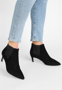 Svarta ankelboots i mocka med spetsiga tår och en låg stilettklack. Har elastiska sidor och en elegant design.