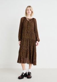 Brūna ziedu kleita ar garām piedurknēm, ar sasienamu dekoltē, slāņainu apakšmalu un caurspīdīgu audumu. Nēsā ar melnām kurpēm un baltām zeķēm.