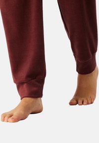 Bordeauxfarbene Sweatpants mit gerippten Bündchen, aus weichem Stoff gefertigt. Ein barer Fuß ist neben dem Hosenbein sichtbar.