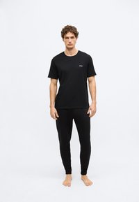 Μαύρο T-shirt με μικρό λευκό λογότυπο "BOSS", σε συνδυασμό με μαύρο παντελόνι στενής γραμμής. Και τα δύο ρούχα έχουν λεία υφή και άνετη εφαρμογή.