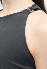 Κοντινό πλάνο ενός ατόμου που φοράει αμάνικο τοπ σκουρό γκρι με ασημένιο κούμπωμα στον ώμο.