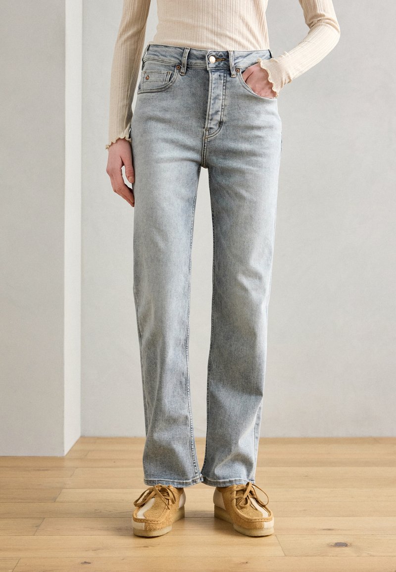 Jeans straight leg in lavaggio chiaro con vita alta, cinque tasche e un leggero effetto sbiadito. Abbinati a scarpe color sabbia con un design testurizzato.