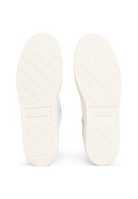 Bílé gumové podešve tenisek s texturovanými úchyty a mřížkami, představující mírně zvýšené logo u paty a hladké okraje.