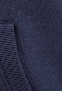 Tela de punto azul marino que muestra una textura suave y un detalle acanalado en el borde, con un aspecto ligeramente difuso.