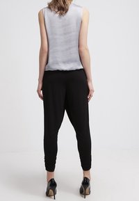 Haut gris sans manches à texture fluide, associé à un pantalon noir fuselé avec des poignets élastiques, et des escarpins noirs élégants.