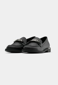 Mustad nahast loafers, millel on lame kummist tald, vampi peal on kettaga aksessuaar ja sile tekstuur. Lihtne, ümar disain.