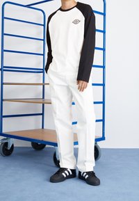 Dlouhý rukáv raglanový tričko v off-white a černé barvě, se znakem na prsou. Doplněno bílými kalhotami a černými teniskami s bílými pruhy.