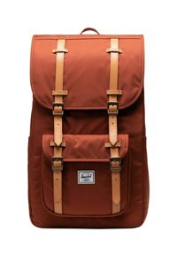 Sac à dos en tissu marron avec des sangles et des boucles en cuir, poche avant et rabat supérieur. Présente une étiquette de marque à l'avant.