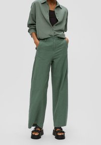 Zelená, strukturovaná košile s knoflíky, spojená s širokými, vysokými kalhotami. Černé sandály mají platformu a akcenty v podobě mašlí.