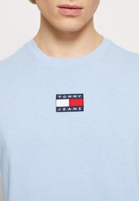 Ljust blå bomulls t-shirt med rund hals, med en rektangulär broderad logopatch i marinblått, vitt och rött som säger "TOMMY JEANS."