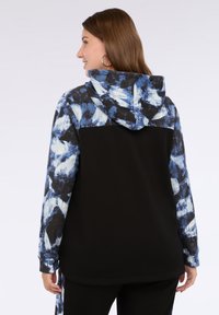 Felpa con cappuccio caratterizzata da un corpo nero e maniche e cappuccio con motivo tie-dye blu. Tessuto morbido con vestibilità rilassata e spacchi laterali.