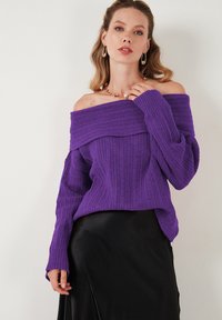 Maglione viola a spalle scoperte con maniche lunghe, lavorazione a coste, con un ampio scollo e una vestibilità rilassata, abbinato a una gonna nera.