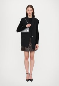 Svart oversize blazer väst, svart långärmad topp, brunt läder mini kjol, silverhandväska, svarta spetsiga klackar, minimalistisk design.