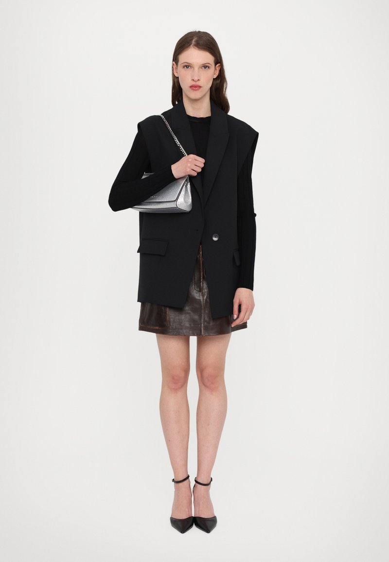 Svart oversize blazer väst, svart långärmad topp, brunt läder mini kjol, silverhandväska, svarta spetsiga klackar, minimalistisk design.
