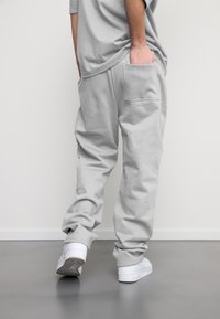 Pantaloni joggeri gri deschis, din bumbac moale, cu un buzunar pe partea dreaptă și o croială relaxată, asortați cu adidași albi.