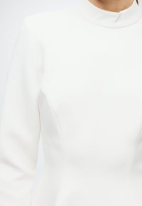 White high-neck dress featuring long sleeves and structured, tailored design. Smooth texture with subtle seam detailing.