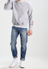 Grå crewneck-tröja med röda grafiska tryck på ärmarna, i kombination med ljusblå jeans och vita sneakers, med uppvikta ärmar och avslappnad passform.