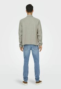 Lässige graue Jacke mit Kragen, kombiniert mit hellblauen Jeans. Das Outfit zeichnet sich durch ein lässiges Design und strukturierte Stoffe aus. Braune Sneakers runden den Look ab.