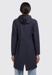 Giacca impermeabile leggera di colore blu navy con cappuccio, maniche lunghe e vita cinchata. Presenta un'etichetta con logo sul colletto posteriore e un orlo dritto.