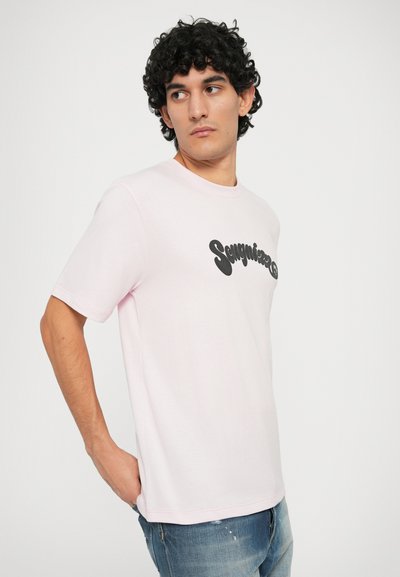 Lichtroze katoenen t-shirt met ronde hals, korte mouwen en zwart golvend textuele afbeelding over de borst. Gemaakt met versleten blauwe jeans.