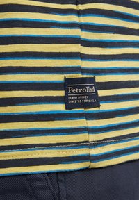 Chemise rayée en jaune, marine et bleu avec une étiquette cousue portant la mention "Petrol Ind" sur le côté gauche. Tissu en coton doux avec une texture lisse.