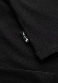 Schwarzes Baumwoll-T-Shirt mit kurzen Ärmeln, glatter Textur und einem kleinen Stoffetikett an der Seite mit dem Markennamen in Weiß.