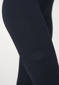 Leggings azul marinho com detalhe em padrão chevron texturizado, apresentando um tecido liso e elástico e uma silhueta ajustada para conforto.