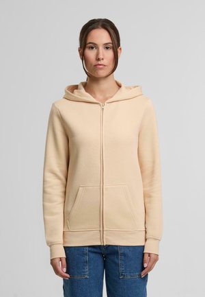 Felpa conzippe color pesca, realizzata in morbido tessuto, con cappuccio, tasche frontali e polsini a coste. Indossata con jeans cargo blu.