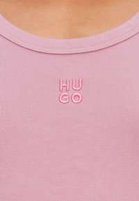 Roze geribbelde tanktop met een geborduurd "HUGO" logo in bijpassend roze. De halslijn is rond en de stof lijkt zacht.