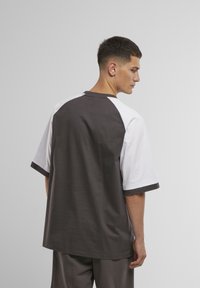 Grijs en witte T-shirt met korte mouwen en een ronde halslijn, met contrasterende raglanmouwen en een matte textuur, weergegeven vanuit de achterkant.