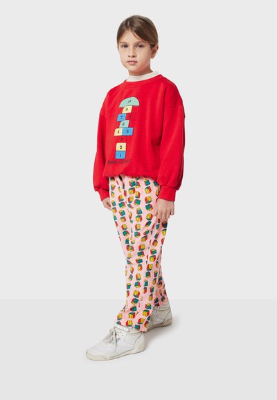 Felpa rossa con grafica colorata a campana e testo. Pantaloni rosa con stampe colorate di case. Sneakers bianche.