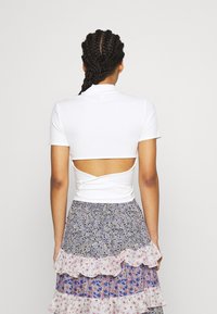Hvid ribbet kortærmet top med bagcut-out detalje, parret med en lagdelt blomstermønstret nederdel med rynkede kanter og varierende farver.