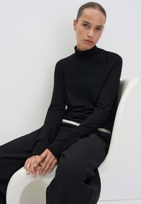 Schwarzes Langarm-Turtleneck-Oberteil aus einem glatten, elastischen Stoff, kombiniert mit lockeren schwarzen Hosen. Minimalistisches Design, ohne Muster.