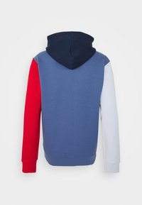 Hooded sweatshirt with a navy hood, blue body, red left sleeve, and light gray right sleeve. Smooth texture, pullover design.