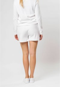 Witte lange mouwen top en bijpassende shorts, gemaakt van zachte stof. De shorts hebben een elastische tailleband en een losse pasvorm, gecombineerd met witte schoenen.