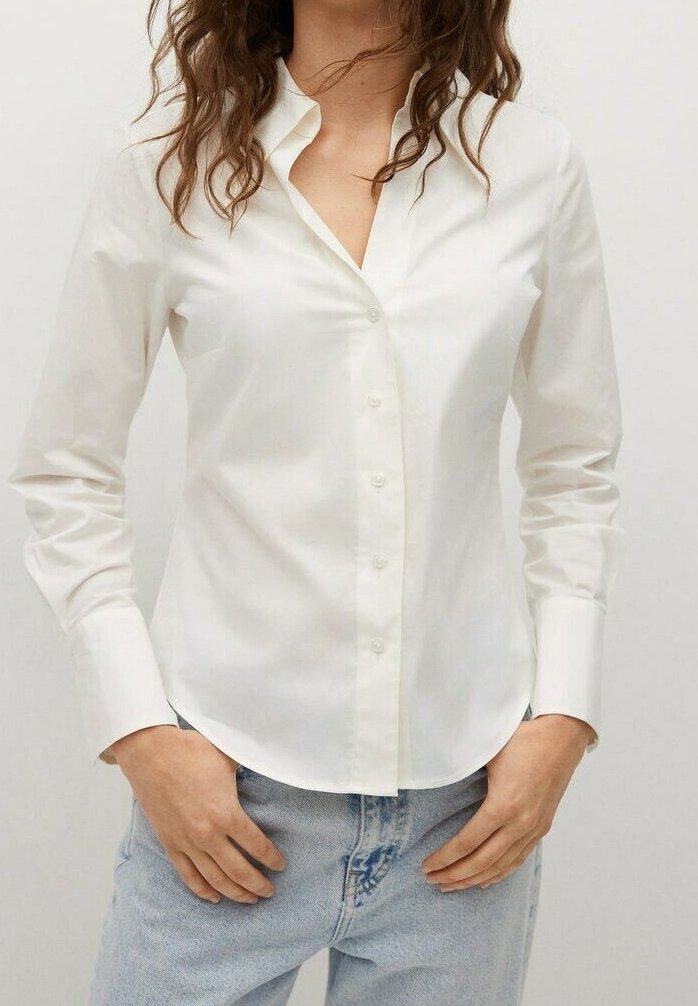 Chemise blanche à manches longues boutonnée avec col, présentant une texture lisse et une coupe ajustée, associée à un jean en denim bleu clair.