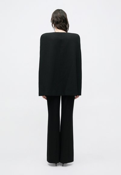 Pikk must kapuutsiga sarnane topp, millel on lai kaelus, kombineeritud kinnimõõdetud mustade lehvivate pükstega. Sile kangas ja õmblusteta disain kogu komplekti ulatuses.