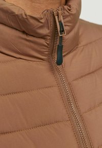 Brūns pūkains veste ar augstu apkakli, centrālais rāvējslēdzis, gluda tekstūra un smalka režģa raksts uz auduma.