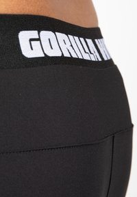 Zwarte sportieve shorts met een brede elastieken tailleband waarop de tekst "GORILLA WEAR" in witte letters staat. Glad fabric met een strakke pasvorm.