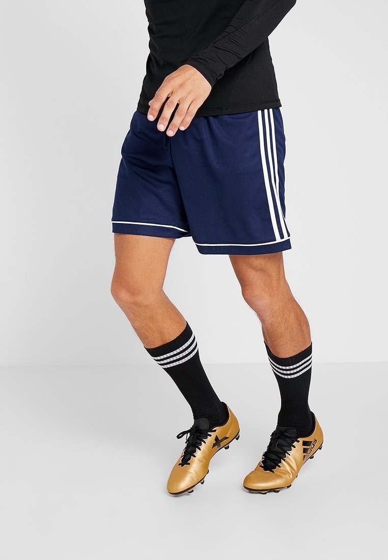 Shorts de sport bleu marine avec bordure blanche, assortis à des chaussettes noires montantes avec des rayures blanches, et des crampons de football dorés.