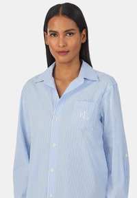 Camicia azzurra a righe con bottoni, dotata di taschino sul petto con logo. Design con colletto e maniche lunghe con dettagli a bottone. Tessuto morbido.