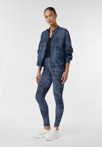 Blue leopard print jacket and matching leggings made of stretchy fabric. Model wears white sneakers, showcasing a casual athletic style.