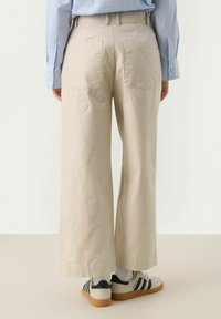 Beige wide-leg trousers with a high waist, two back pockets, and a folded hem, paired with gray and black sneakers.
